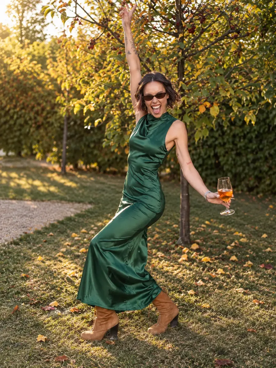 Sare Bare in an emerald green dress, arm raised and laughing in golden autumn light